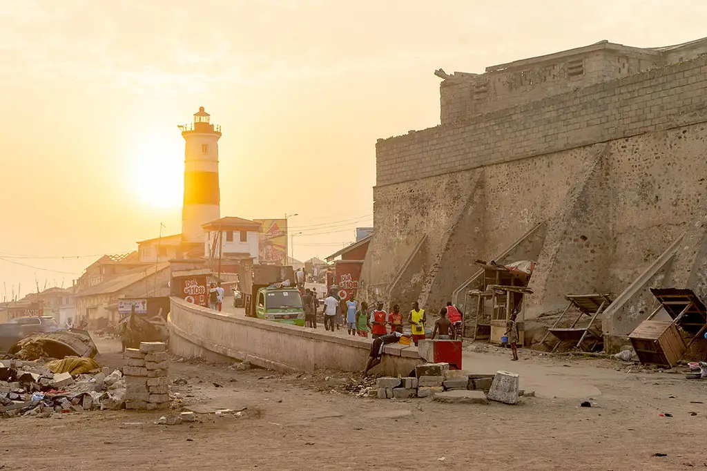 Sunset over Jamestown Fort and its lighthouse in Accra, Ghana, with a busy coastal street market in the foreground