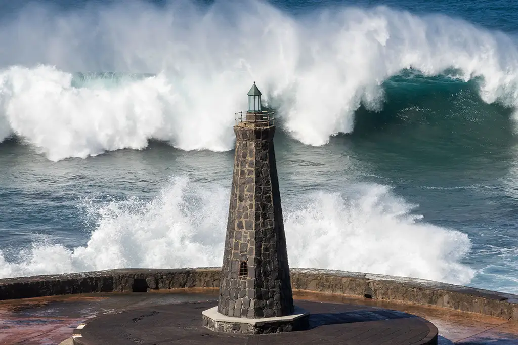 Enormous wave crashing over a small stone lighthouse on the coast of Tenerife, Canary Islands